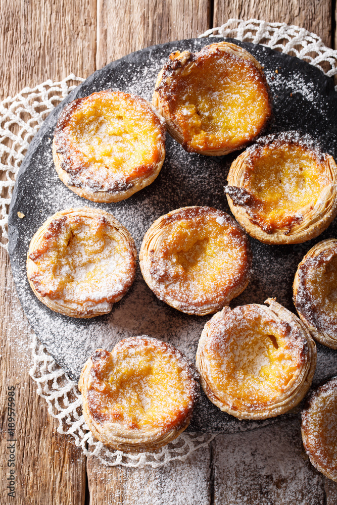 Pastel de nata with sugar powder close-up on the table. vertical top view Pastel de nata with sugar powder close-up on the table. vertical top view