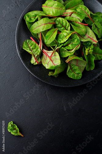 Fresh young leaves of chard for salad in a dark ceramic dish on black concrete background. Selective focus. Copy space. Top view.