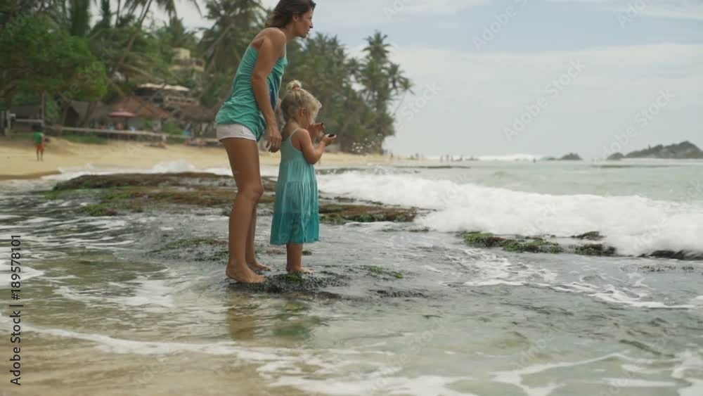 Mother with her daughter enjoy waves staying on stone sunset rapid slow motion Mother with her daughter enjoy waves staying on stone sunset rapid slow motion