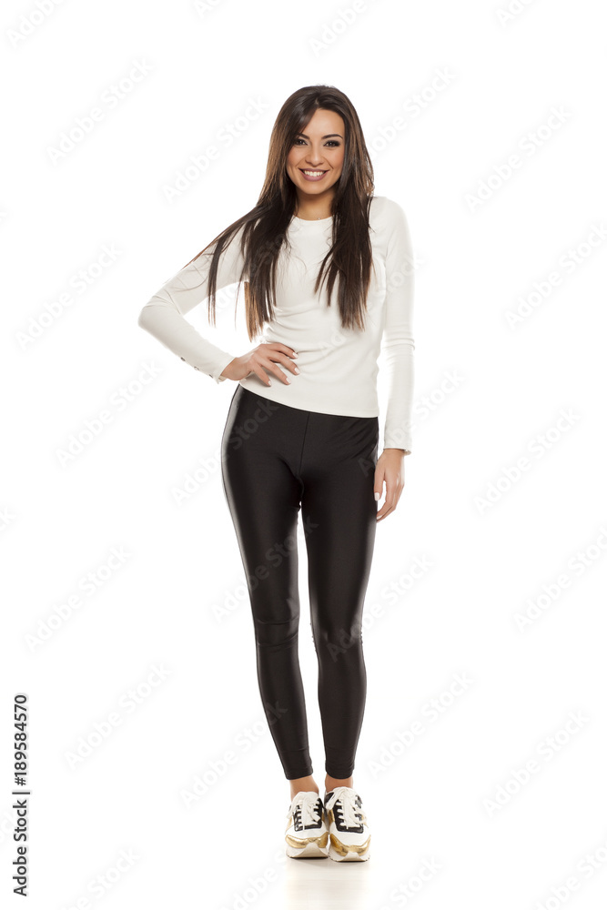 Young beautiful woman in black tights, white blouse and sneakers on white background Young beautiful woman in black tights, white blouse and sneakers on white background