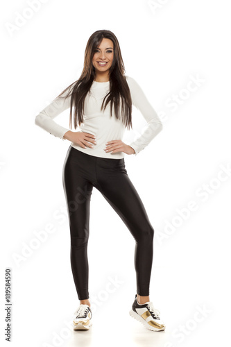 Young beautiful woman in black tights, white blouse and sneakers on white background