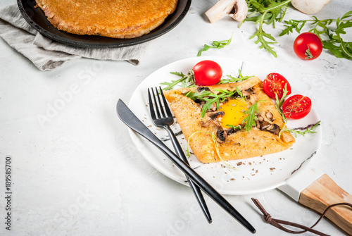 French cuisine. Breakfast, lunch, snacks. Vegan food. Traditional dish galette sarrasin. Crepes with eggs, cheese, fried mushrooms, arugula leaves and tomatoes. On a white concrete table. Copy space