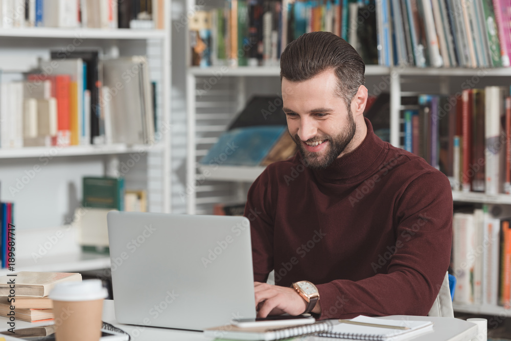 smiling handsome student using laptop in library smiling handsome student using laptop in library