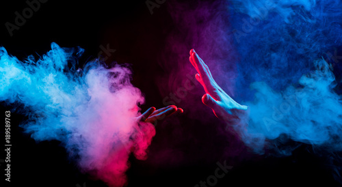 hands reaching from colorful smoke on black background photo