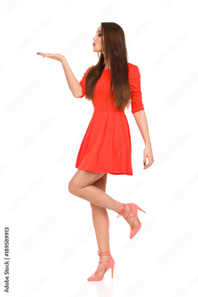 Woman In Red Mini Dress Is Standing On One Leg, Holding Hand Raised And Blowing Kiss Woman In Red Mini Dress Is Standing On One Leg, Holding Hand Raised And Blowing Kiss