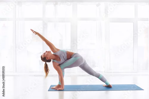 Fototapeta Beautiful young woman practices yoga asana Parivritta Parshvakonasana - Revolving side angle posture at the yoga studio