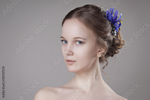 The girl with Nude make-up and hair in wedding bun with flowers on gray isolated background close-up