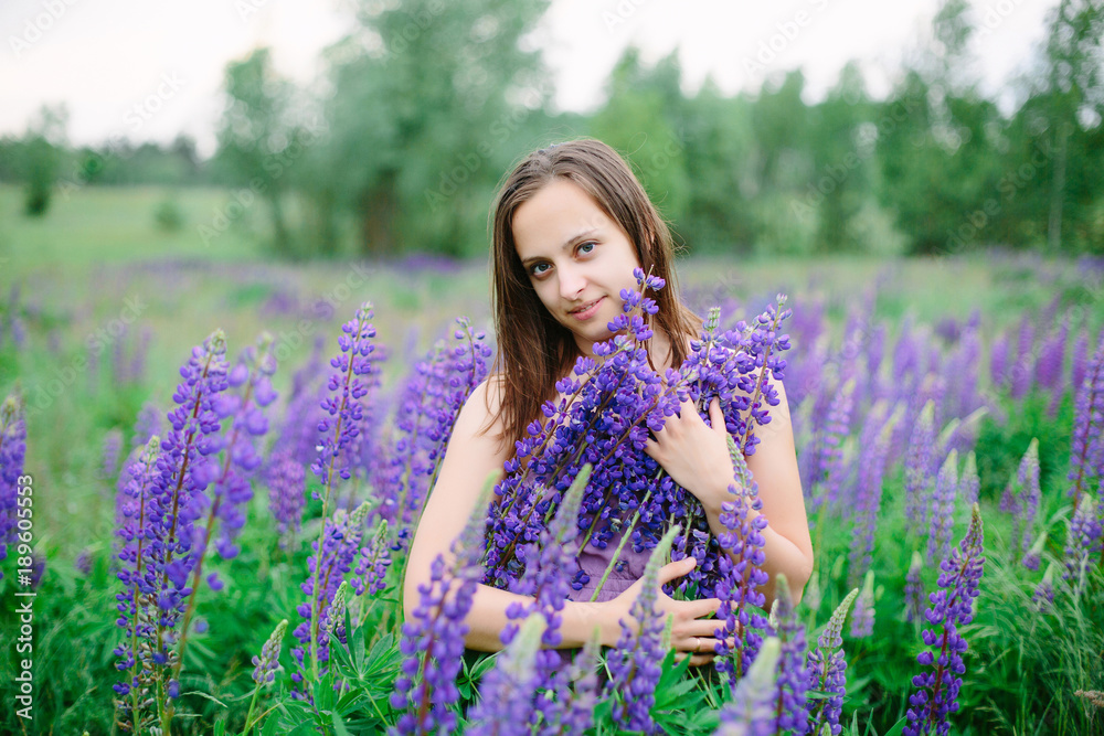 Beautiful young girl in ultra violet dress holding a bouquet of lupine at sunset on the field. The concept of nature and romance. Beautiful young girl in ultra violet dress holding a bouquet of lupine at sunset on the field. The concept of nature and romance.