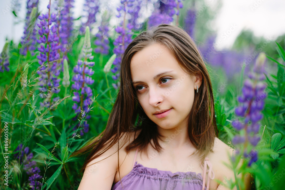 Beautiful young girl in ultra violet dress holding a bouquet of lupine at sunset on the field. The concept of nature and romance. Beautiful young girl in ultra violet dress holding a bouquet of lupine at sunset on the field. The concept of nature and romance.