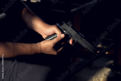 Close up, Hand of a man carrying a magazines gun. There is a bullet in the chamber. Prepare to used protect yourself. He dodged in a dark room with sunlight. Blur and soft focus. 
