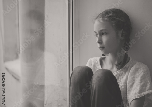 Sad little girl sitting near the window. Black and white.