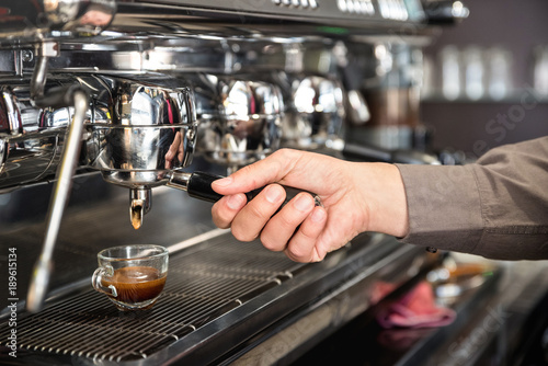 Classic barman hand preparing italian espresso at modern coffee bar machine in fashion cafeteria - Food and beverage concept with professional bartender at cafe stand working station photo