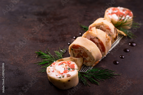 Rolls of thin pancakes with salmon, horseradish cream cheese. Black old background. Top view. Selective focus photo