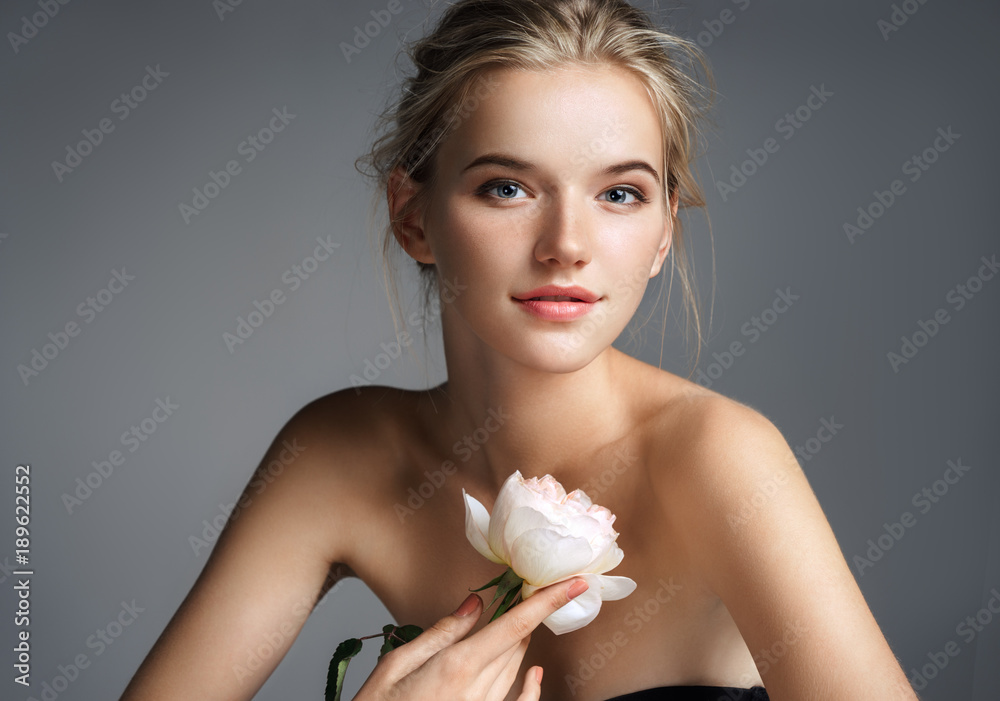 Beautiful young lady with natural make up. Photo of blonde girl with rose on grey background. Skin care concept