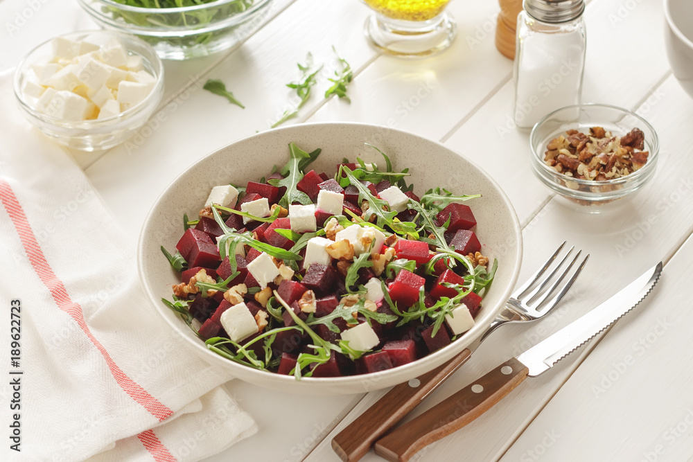 Bowl of vegetable salad with feta cheese on white wooden dinner table.