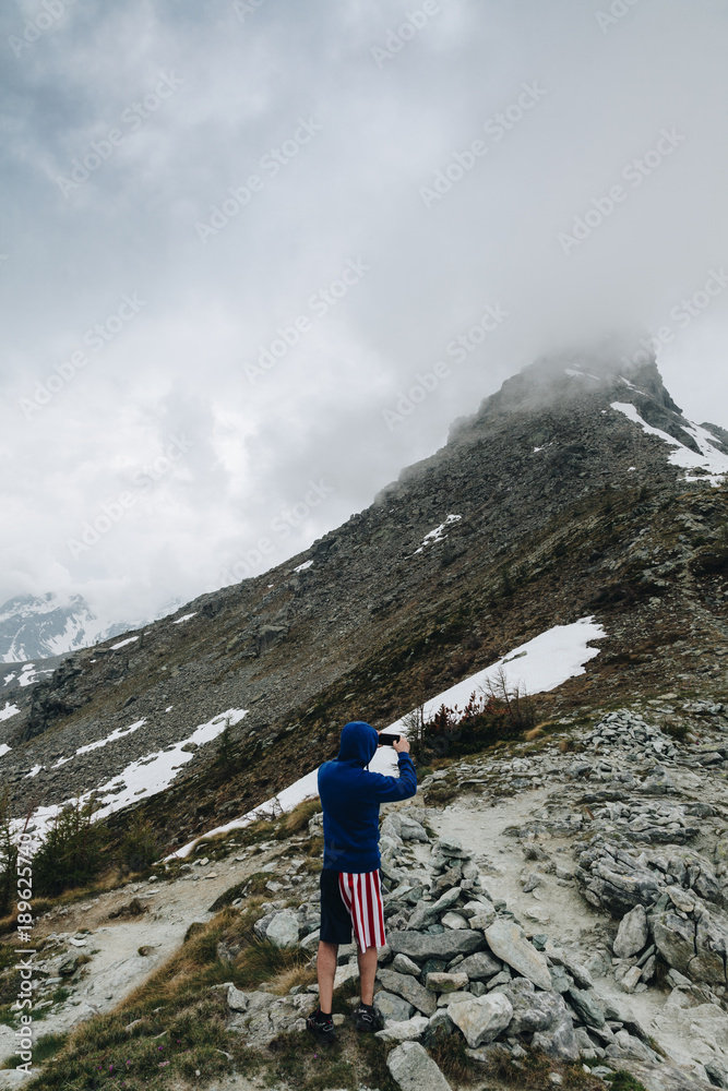 Hiker with short pant American Flag Taking photo with his smart phone to the panorama in the mountain.