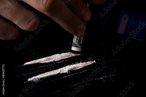 Drug addiction. Junkie man sniffs a line of cocaine through a dollar. Black background. Narcotics concept. photo