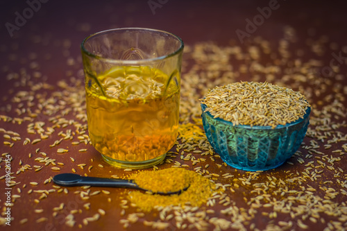 Cumin,Cuminum cyminum with its powder and its extracted water on brown wooden surface.