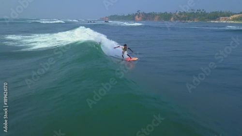 Aerial surfer rides blue ocean wave at sunset drone footage