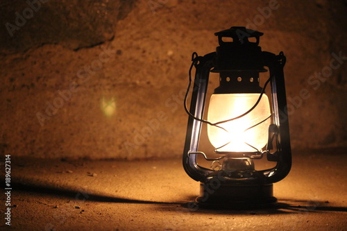 Kerosene lamp lights in a dark near a stone wall. © nebuvo