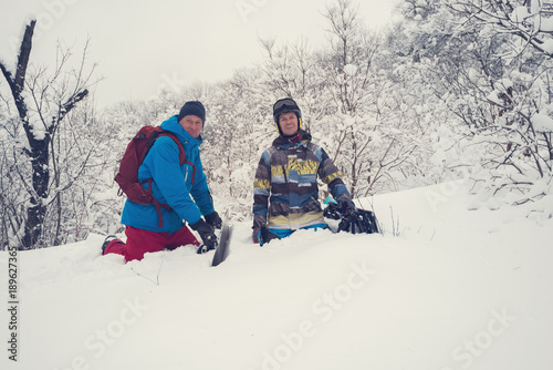 Happy snowboarders are sitting in deep snow after freeride