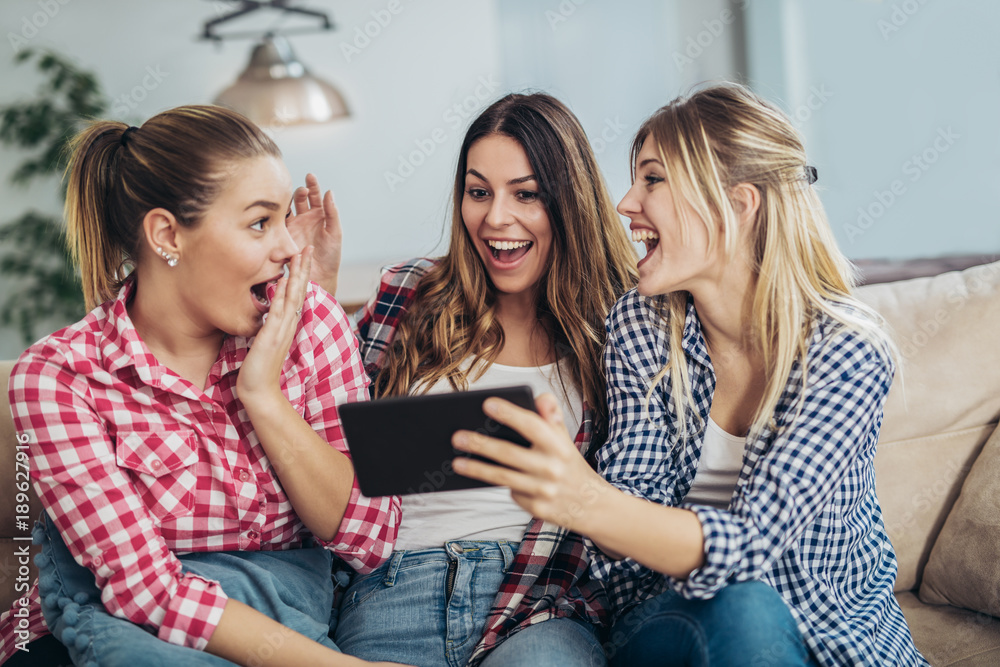 Three best friends using digital tablet together. Women sitting on sofa having fun surfing on the internet using smart digital pc tablet modern device Three best friends using digital tablet together. Women sitting on sofa having fun surfing on the internet using smart digital pc tablet modern device