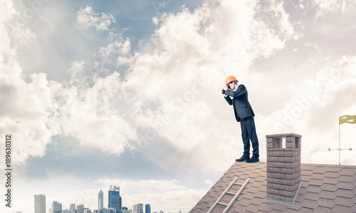Engineer man standing on roof and looking in binoculars. Mixed m