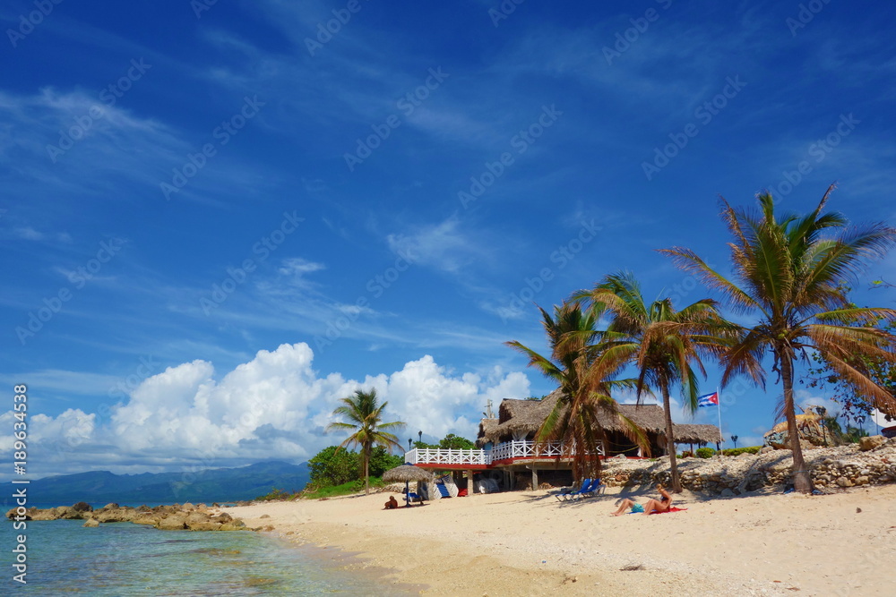 Tropical sandy beach with Cuban flag and a traditional Cuban house surrounded by palm trees, Playa Ancon, Trinidad, Cuba, Caribbean Islands