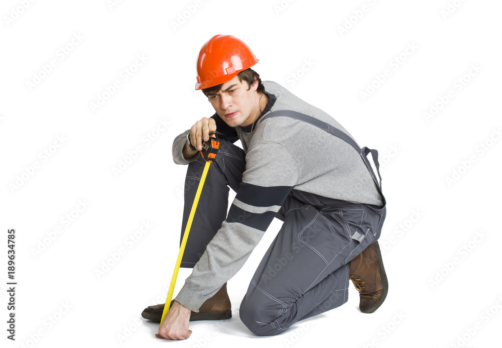 A young man in working grey clothes and orange hard helmet measuring the metric area in the room. A young man in working grey clothes and orange hard helmet measuring the metric area in the room.