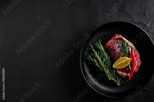 Raw beef steak in spices on a black frying pan for grilling, top view