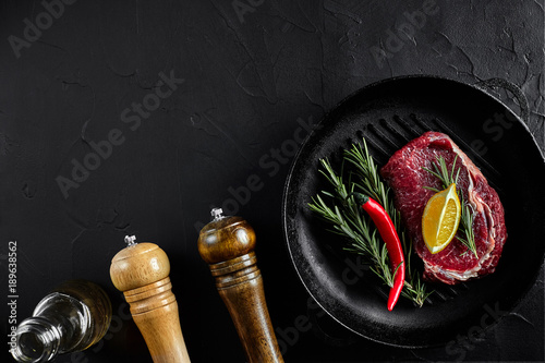 Raw beef steak in spices on a black frying pan for grilling, top view