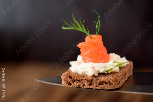 Fototapeta Naklejka Na Ścianę i Meble -  Canape with salmon is lying on a knife on a dark background
