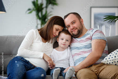 Image of happy pregnant wife, husband and son on gray sofa