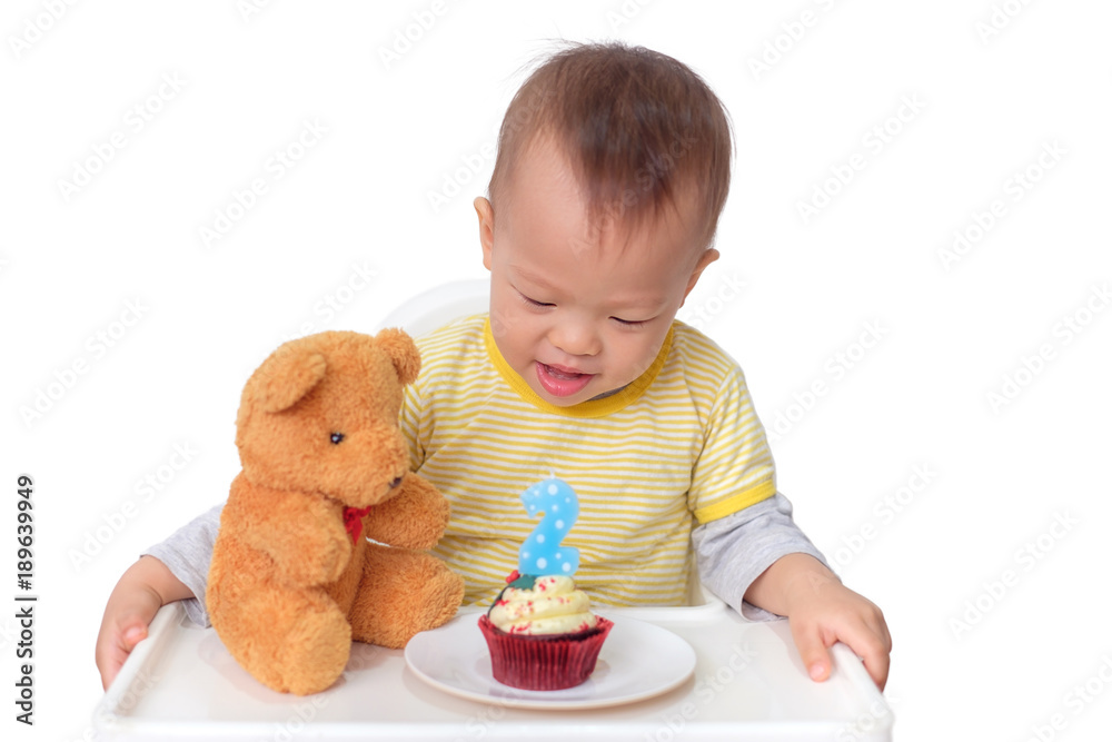 Cute little Asian 2 years old toddler baby boy child sitting in high chair celebrating birthday and blowing candle on red velvet cupcake with teddy bear, isolated on white with clipping path Cute little Asian 2 years old toddler baby boy child sitting in high chair celebrating birthday and blowing candle on red velvet cupcake with teddy bear, isolated on white with clipping path