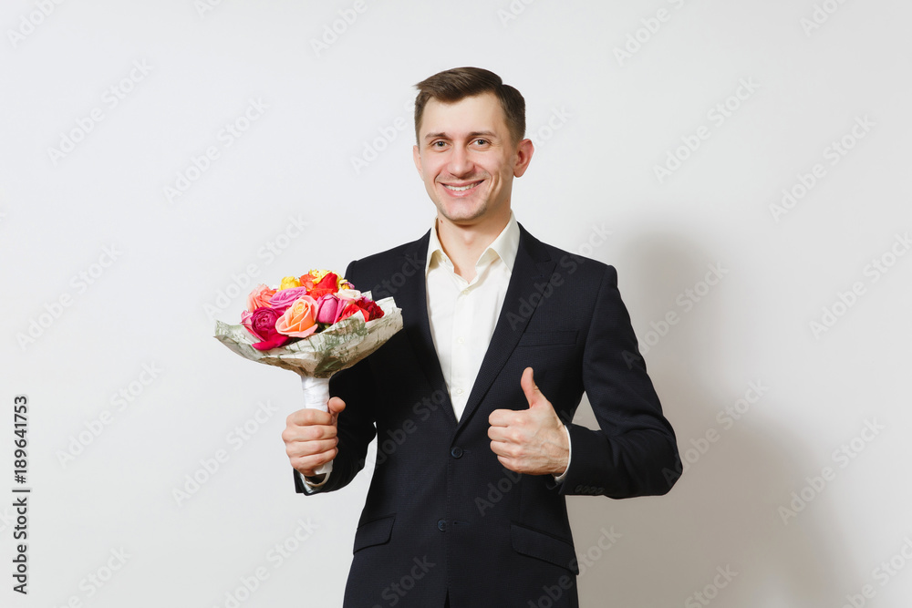 Young handsome smiling man in suit showing thumb up, holding bouquet of beautiful roses flowers isolated on white background. St. Valentine's Day, International Women's Day, birthday, holiday concept. Young handsome smiling man in suit showing thumb up, holding bouquet of beautiful roses flowers isolated on white background. St. Valentine's Day, International Women's Day, birthday, holiday concept.