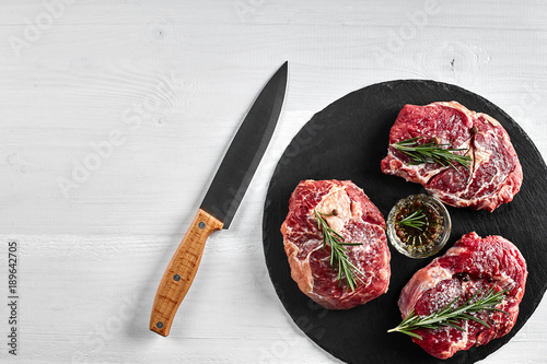 Fresh raw beef steaks with herbs, garlic, olive oil, pepper, salt and rosemary on black board: Tenderloin, Striploin, Rib Eye photo