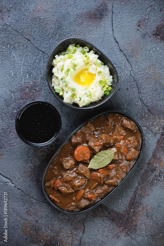 Traditional Irish beer and beef stew served with champ and dark beer for Saint Patrick’s Day, top view over grey asphalt background