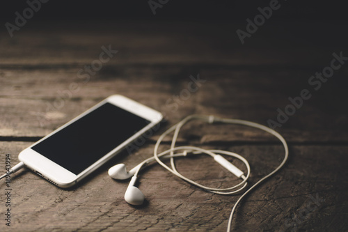 Close-up of smart phone with headphones on a Wood background. Listen to music. vintage Tone
