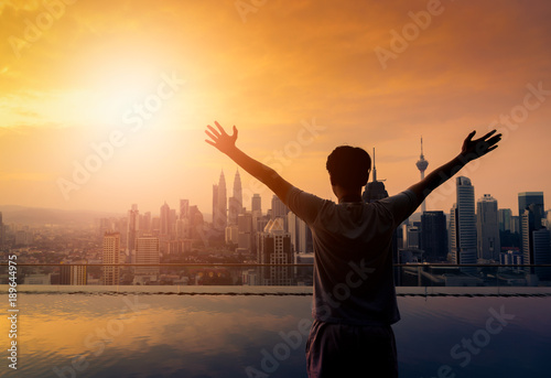 Silhouette Happy man standing near the swimming pool in roof of hotel at sunrise, Kuala Lumpur, Malaysia.