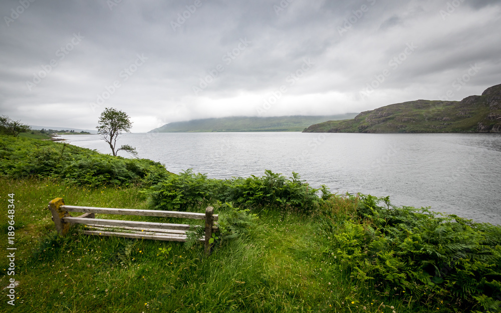 Obraz premium Loch Ewe viewpoint, Highlands, Scotland. A bench looking over the calm waters of Loch Ewe in the Scottish Highlands on a grey and overcast day.