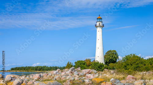 Kihnu island lighthouse in Estonia. Stand alone single white lighthouse stones green forest summer blue sky. photo