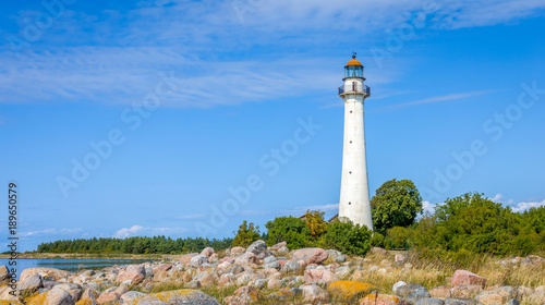 Kihnu island lighthouse in Estonia. Stand alone single white lighthouse stones green forest summer blue sky.