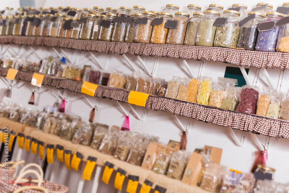 Big choice of glass cans with many different dried spices plants is standing on shelf