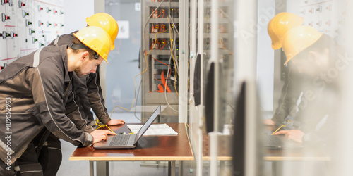 Two maintenance engineers inspect relay protection system with laptop comp photo