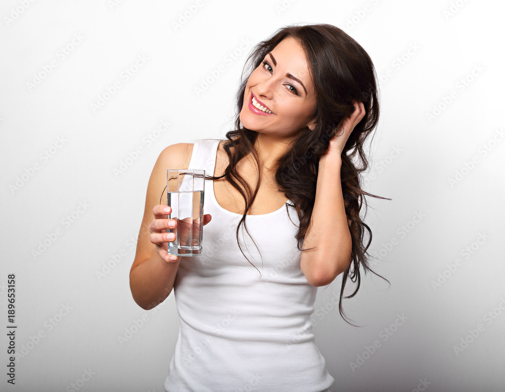 Positive happy toothy smiling woman with long healthy long curly hair holding the glass of pure water on white background Positive happy toothy smiling woman with long healthy long curly hair holding the glass of pure water on white background