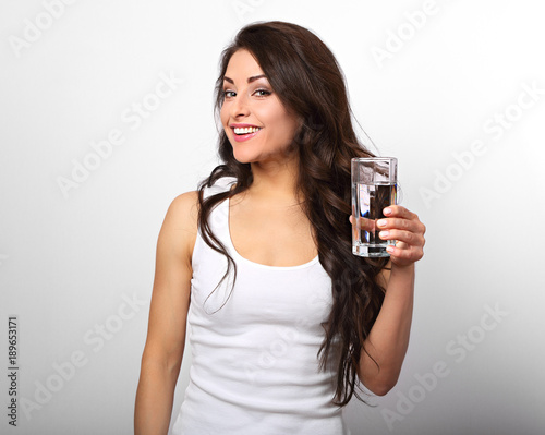Positive happy toothy smiling woman with long healthy long curly hair holding the glass of pure water on white background
