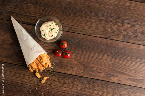 French fries, in a paper bag on a wooden brown background, top view. Fast food.