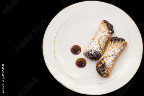 Italian cannoli with chocolate chips on white plate over black background photo