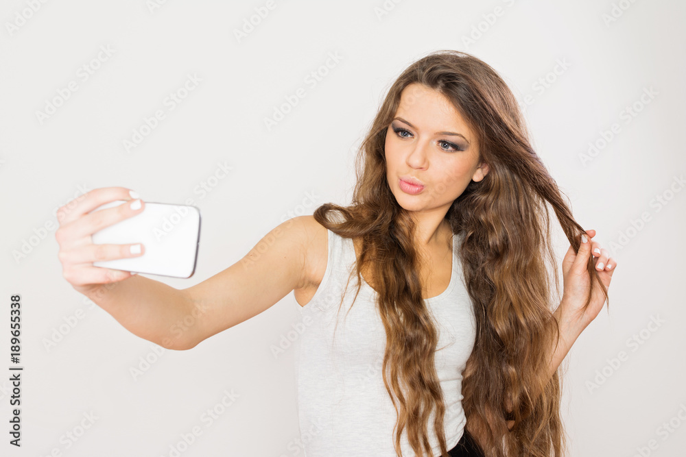 Gorgeous teenage girl with long brown hair taking a selfie on smart phone Gorgeous teenage girl with long brown hair taking a selfie on smart phone