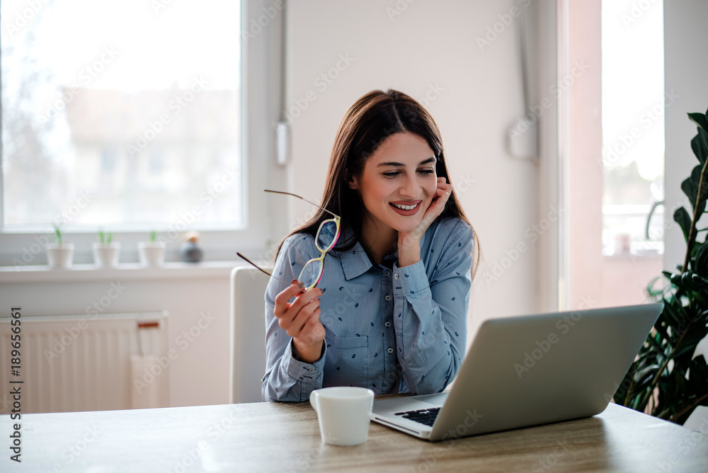 Young female freelance worker holding eyeglasses, sitting at home-office. Young female freelance worker holding eyeglasses, sitting at home-office.